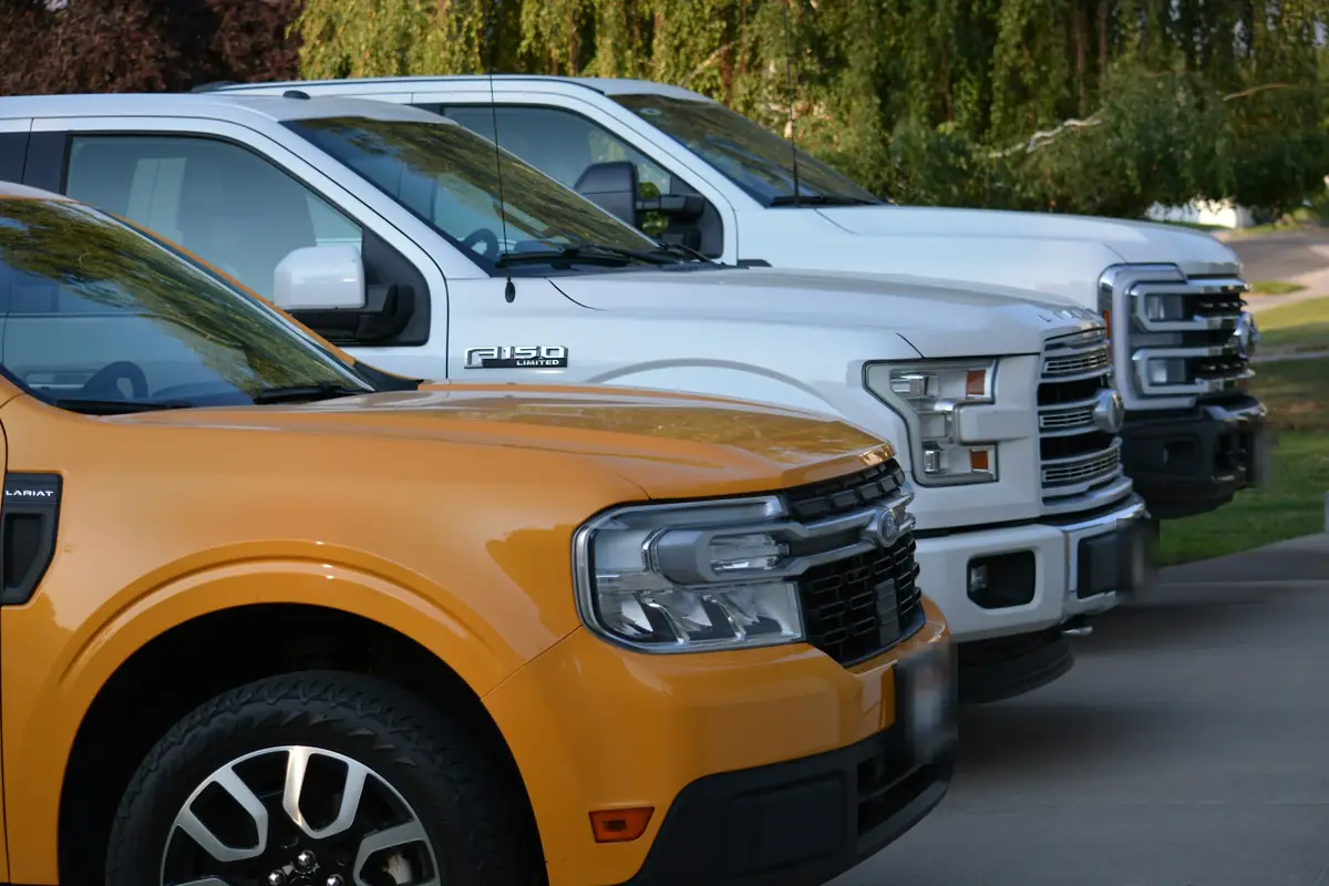 Three pickup trucks parked side by side, an orange compact pickup in front of two white full-size pickups.